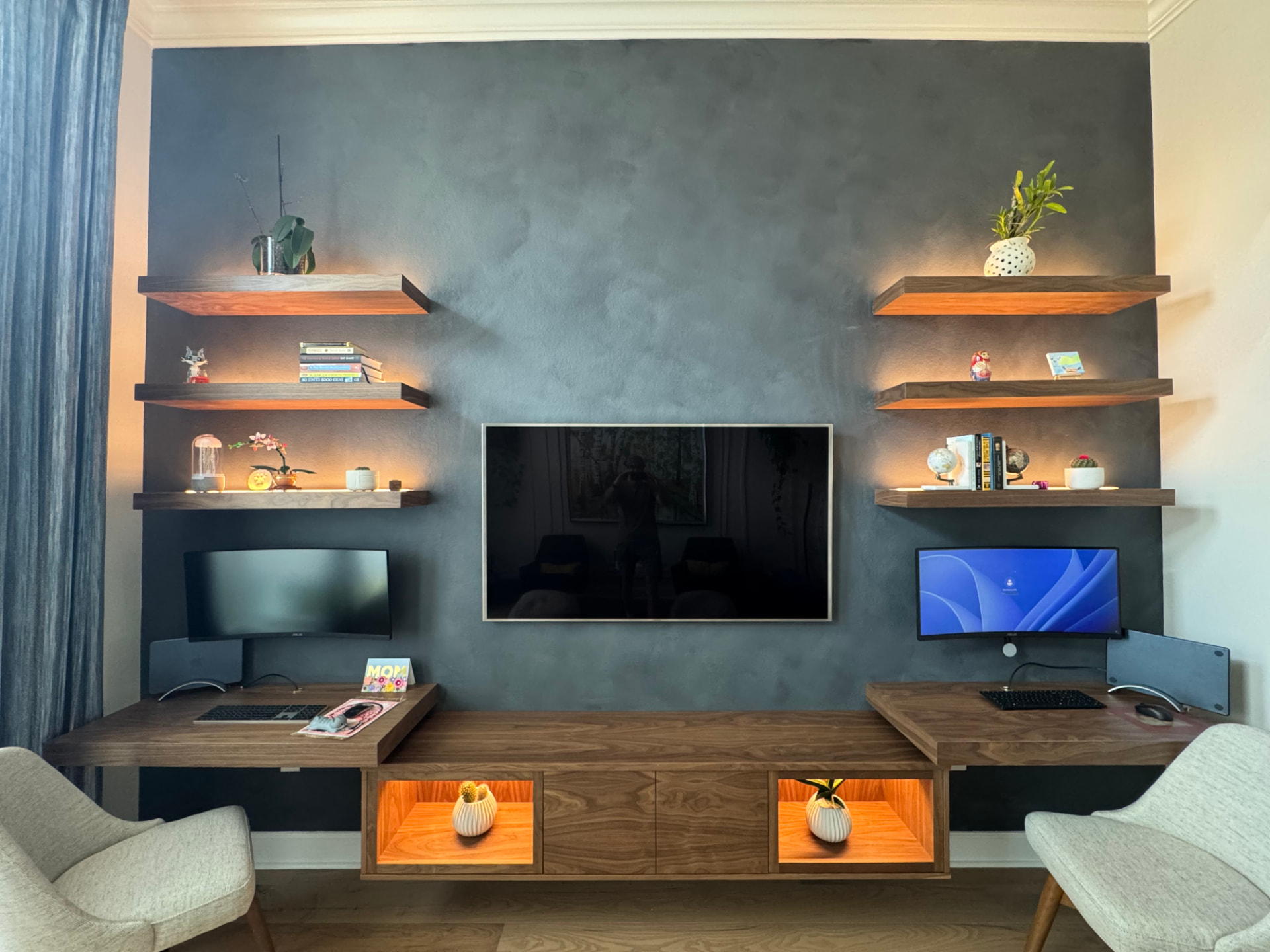 Custom floating walnut media wall with dual built-in desks, lit display niches, and floating shelves
