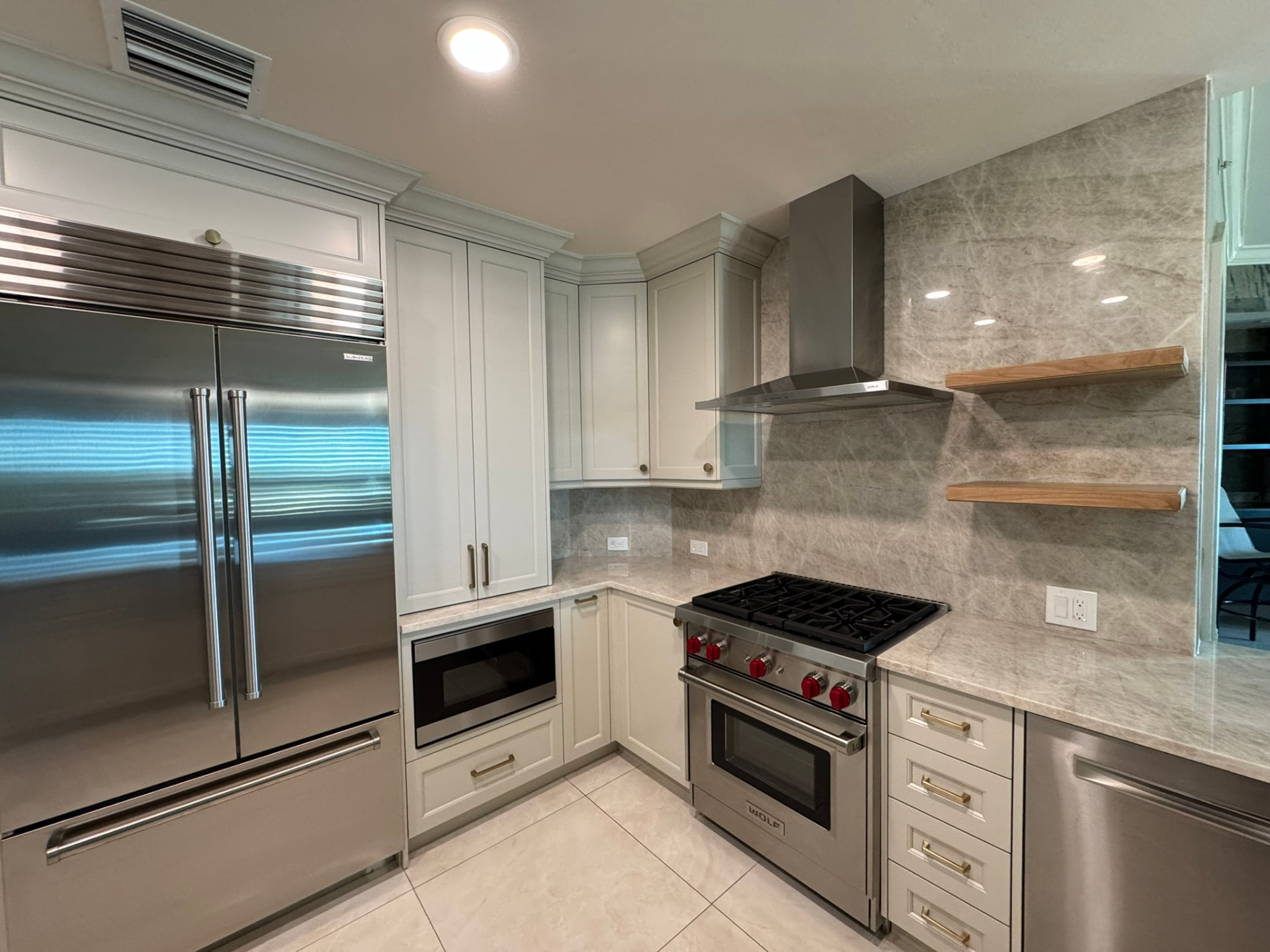 Custom painted kitchen cabinetry with paneled refrigerator surround, Wolf range, and floating wood shelves