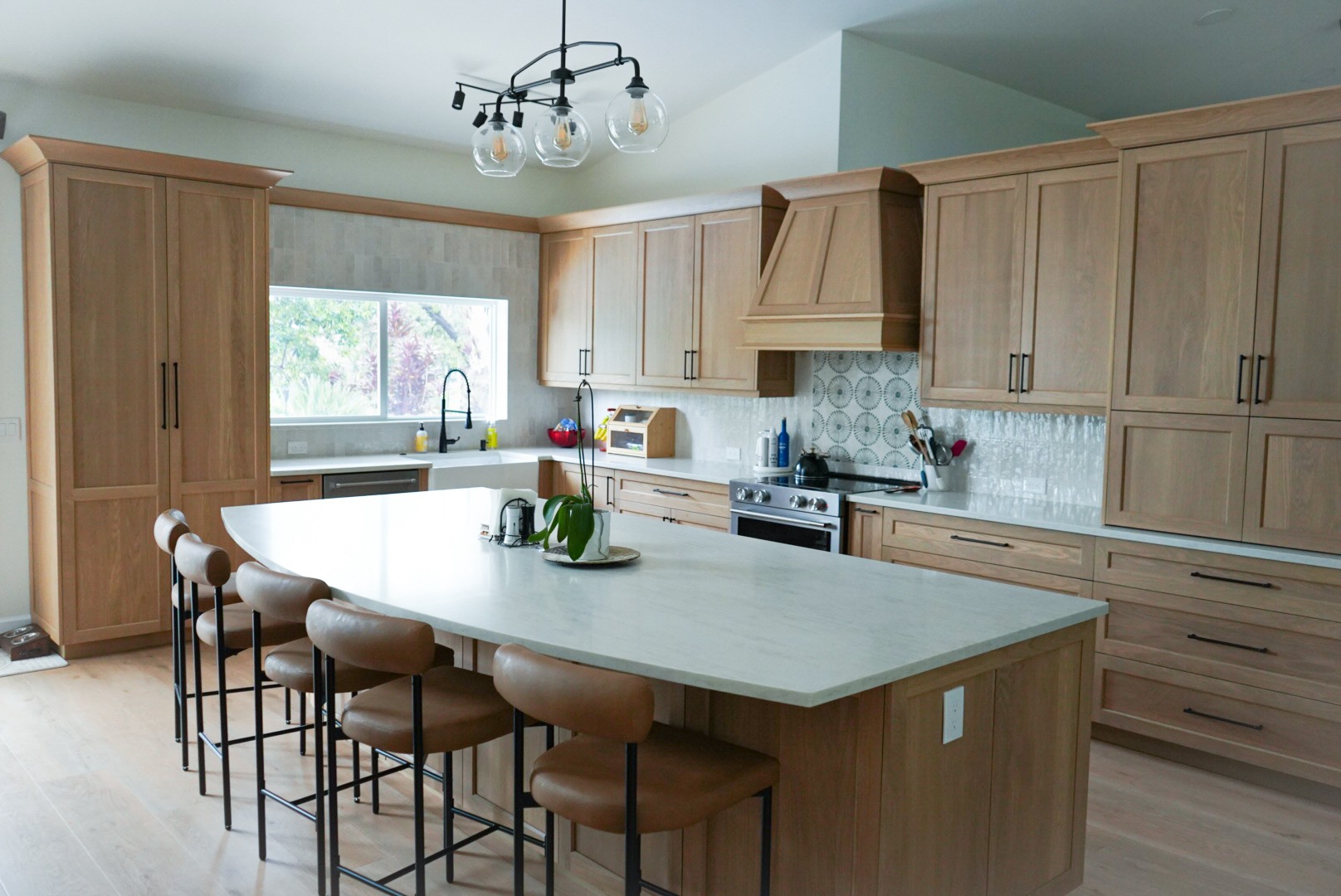 Natural white oak kitchen with custom wood range hood, white marble island with leather bar stools, and pendant lighting